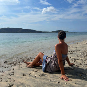 Ein Model sitzt im Sand am Strand und trägt das Pestemal Tarifa in Grau