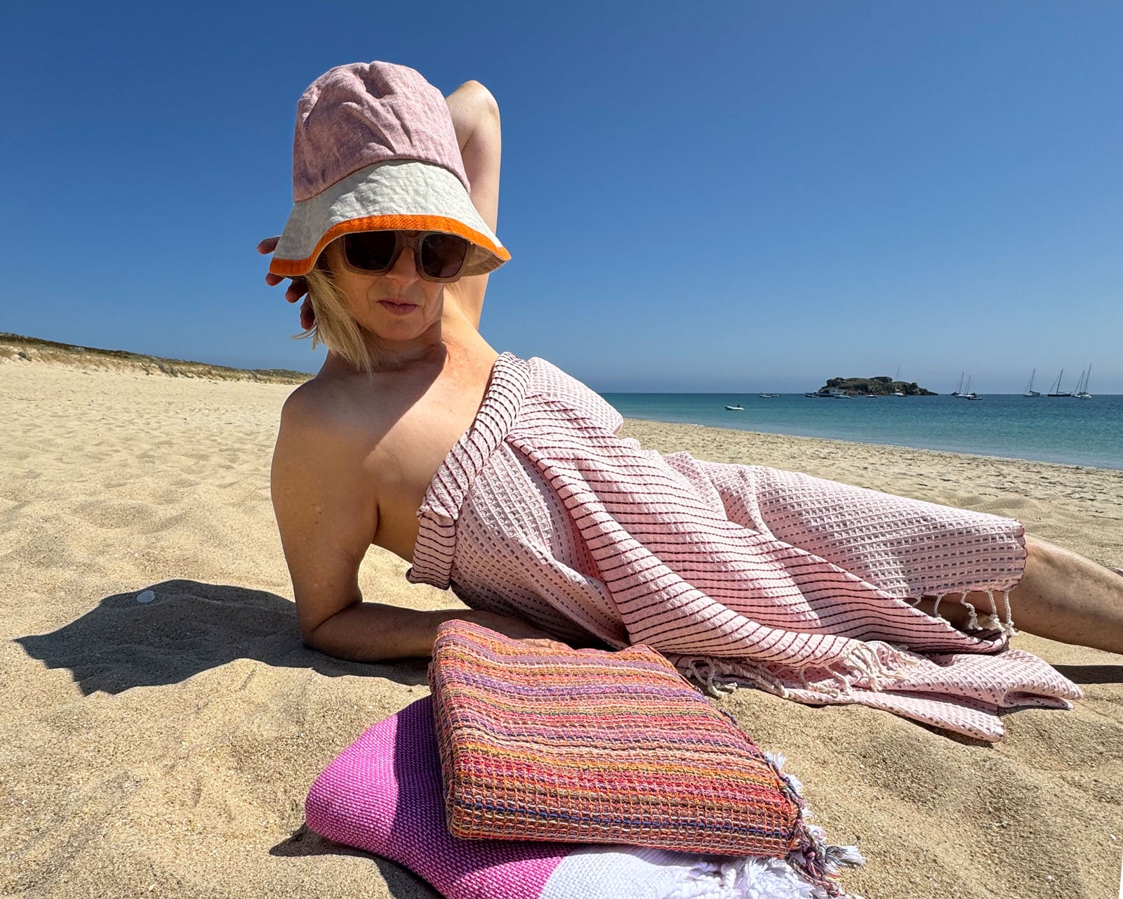 Frau liegt im Sand am Strand mit dem Hamamtuch in Waffelpique Muster in Rot und Rosa